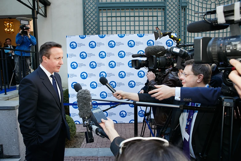 man talking to media while surrounded by cameras and other reporters