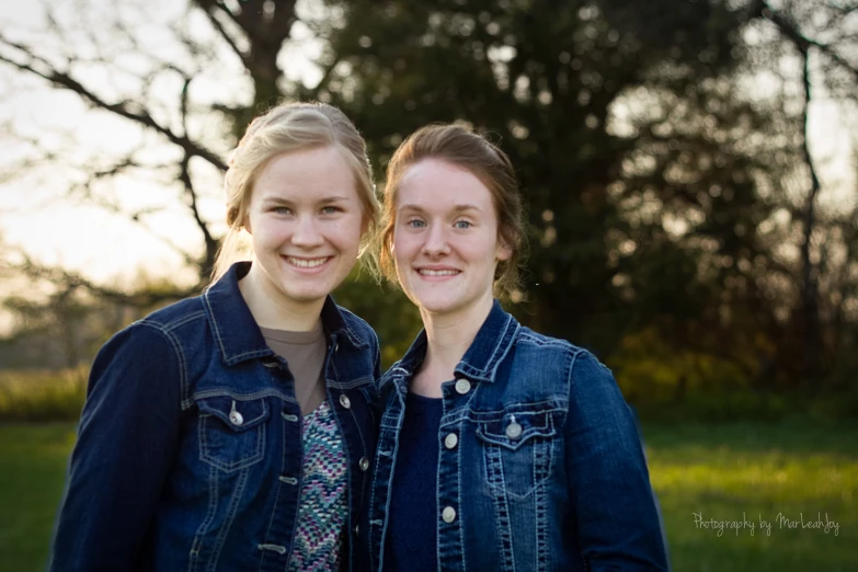 two young women stand in front of trees