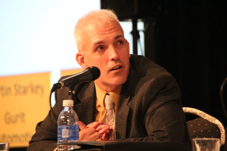 an old man in a suit talking into a microphone