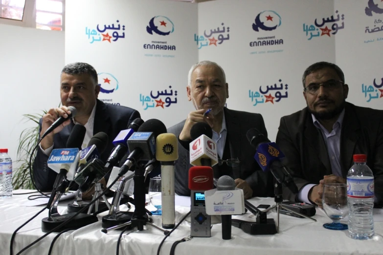 three men sitting at a table with microphones