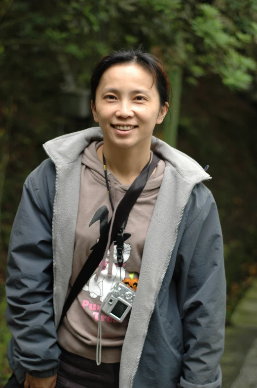 a woman smiles in front of trees while wearing headphones