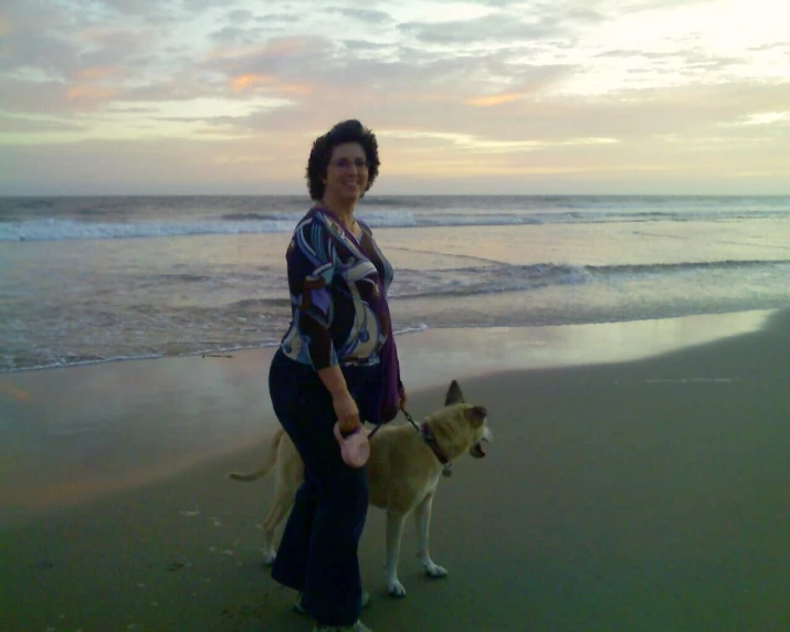 a woman standing on a beach next to her dog