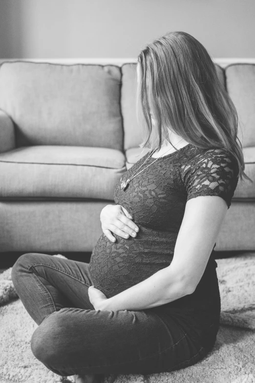 pregnant woman sitting on floor with her belly curled in front of the couch