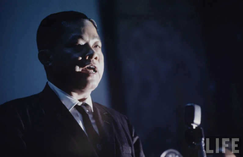 man in suit speaking into microphone in darkened room