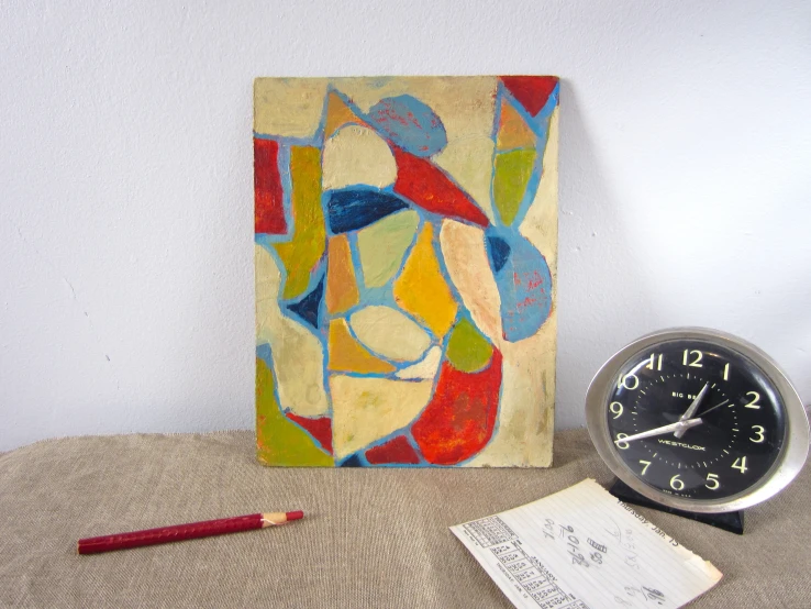 a painting sitting next to an alarm clock and paper