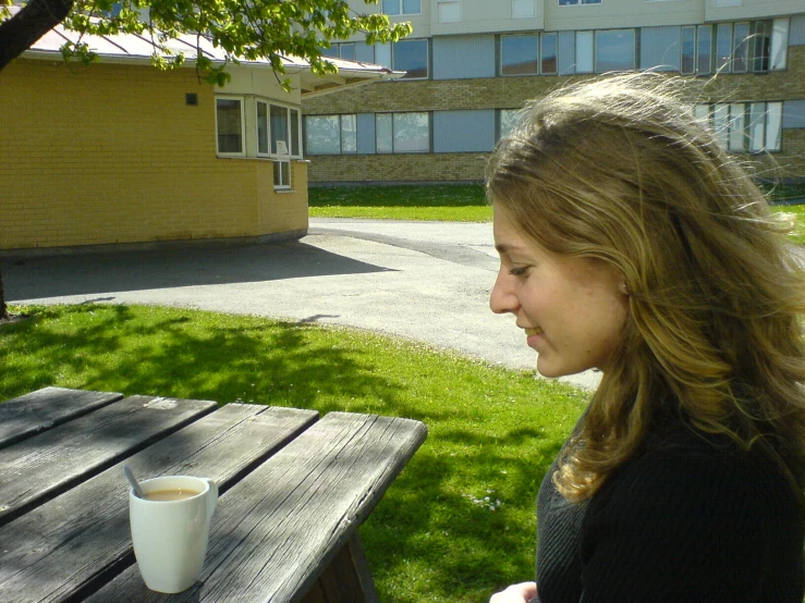 a woman sitting at a picnic table next to a cup of coffee