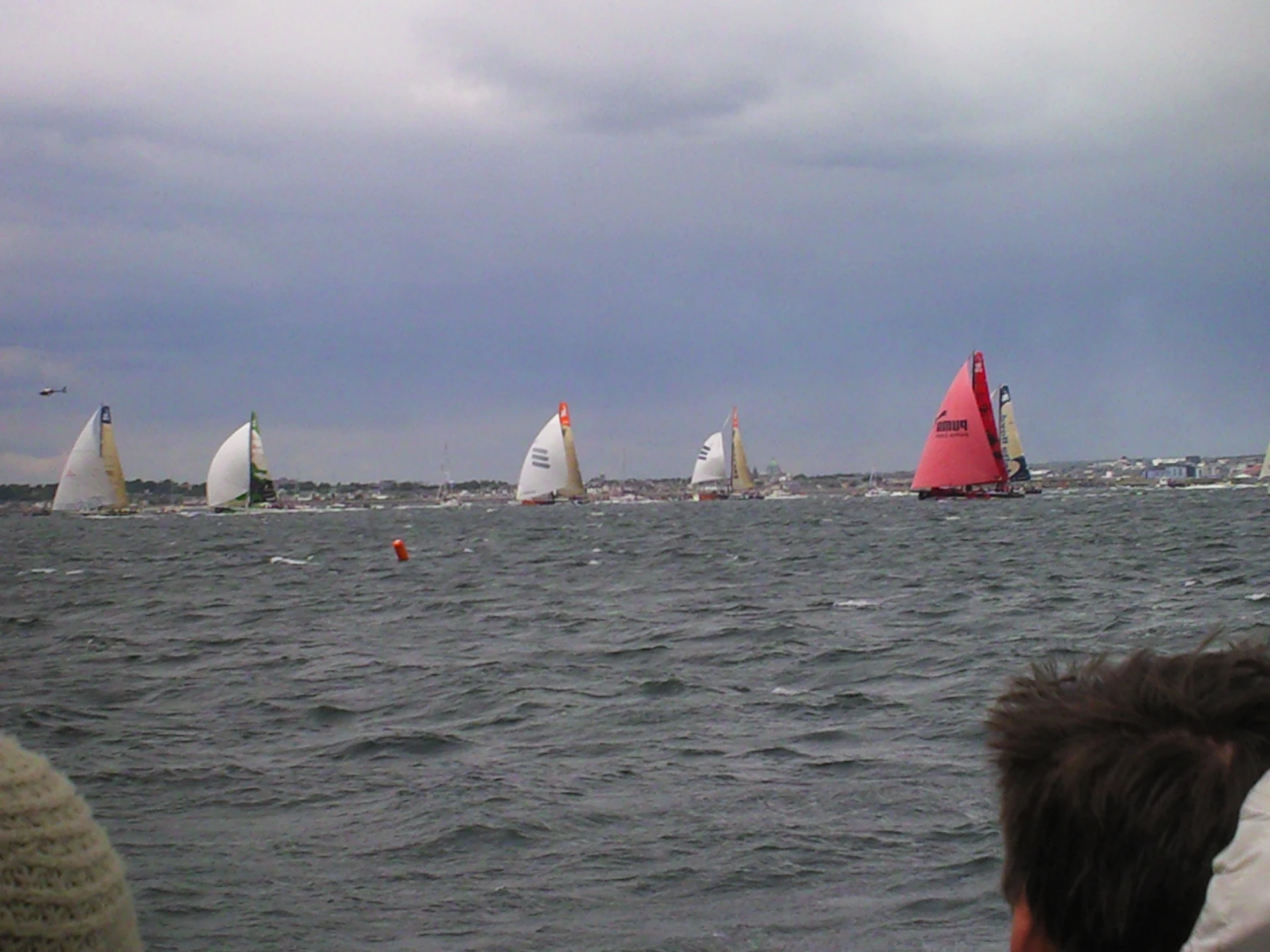 a group of sailboats on the ocean with clouds overhead