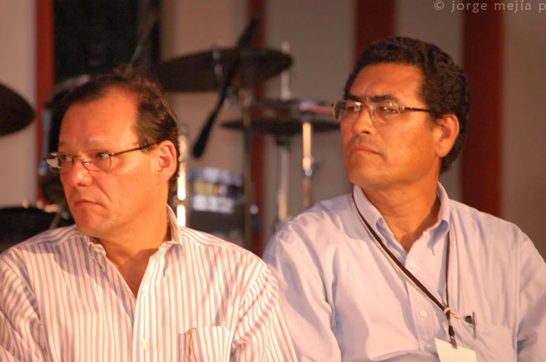 two men with glasses standing in front of a music stand