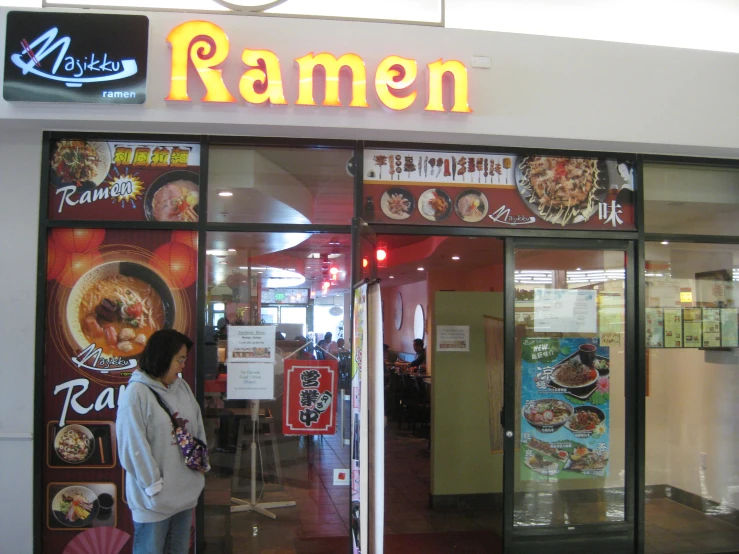 a person standing in front of a building and the window sign reading ramen