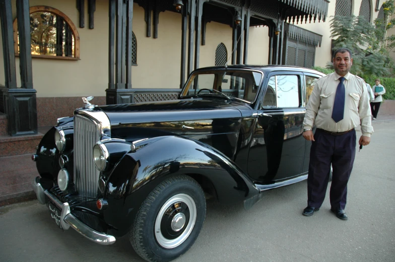 a man in a suit standing next to a black car