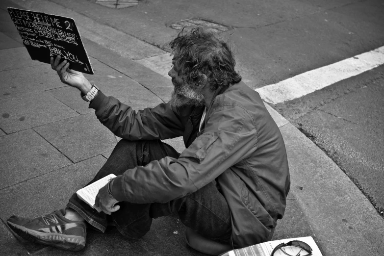 a man sitting on the side walk reading a book