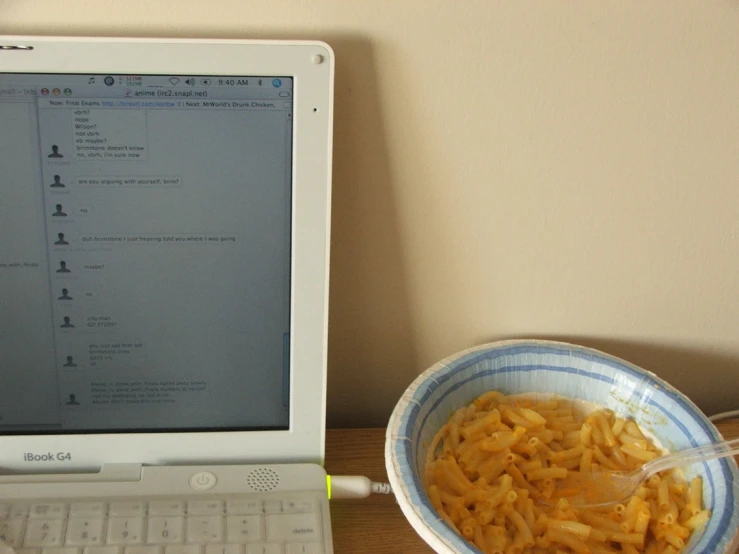 a bowl of noodles sits next to an apple computer