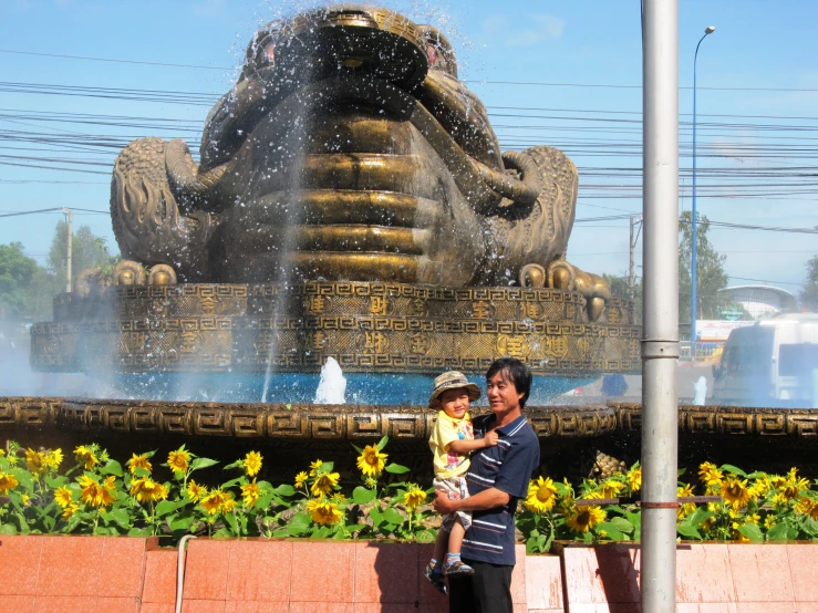 a man holding a baby is near a fountain