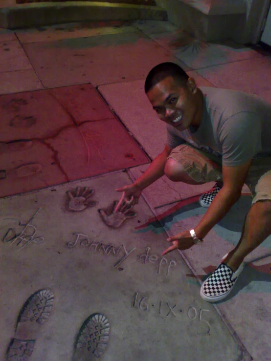 a young man kneeling down on a sidewalk while drawing with letters