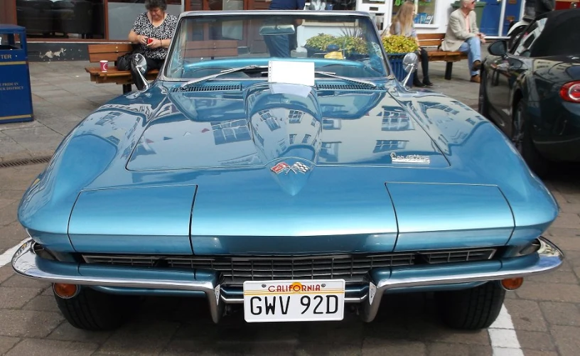 an old blue sports car parked in a lot with people standing around