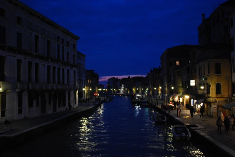 people walk down the sidewalk beside a narrow waterway