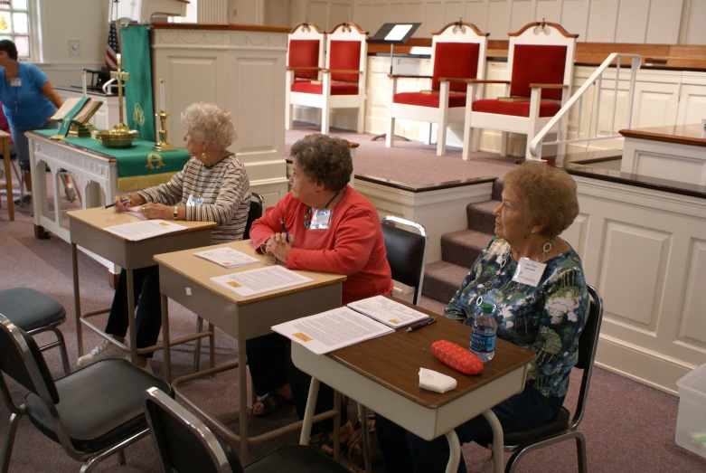 elderly women sitting at desks with chairs in background