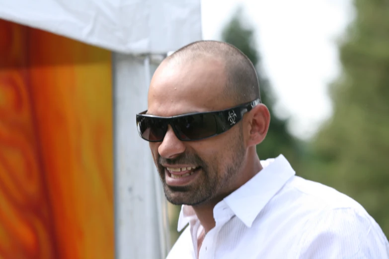 a bald man wearing sunglasses in front of a painting