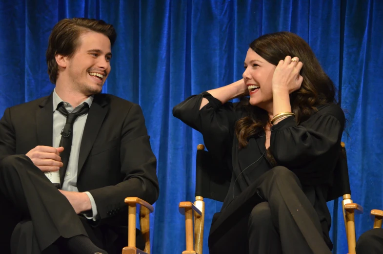 the actors smile while talking together in front of a blue curtain