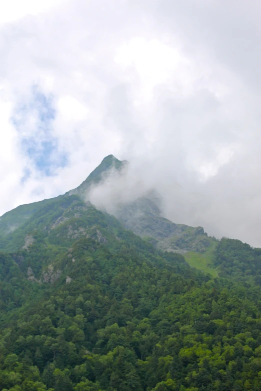 a lush green mountain covered in cloud covered sky