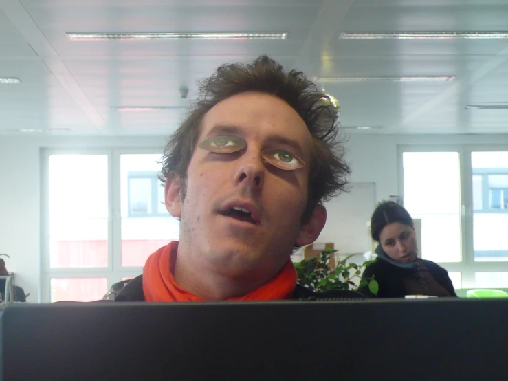 a man with eye glasses, stares through the top edge of a laptop