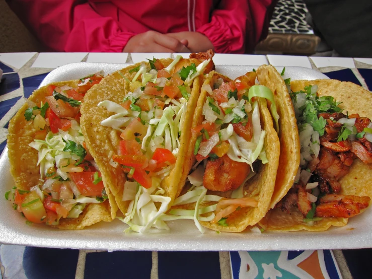 three tacos, a cabbage coleslaw and a tomato on a tray