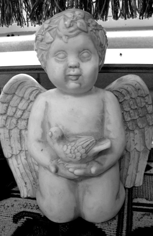 an angel statue sitting on the floor with a small bird in its arms
