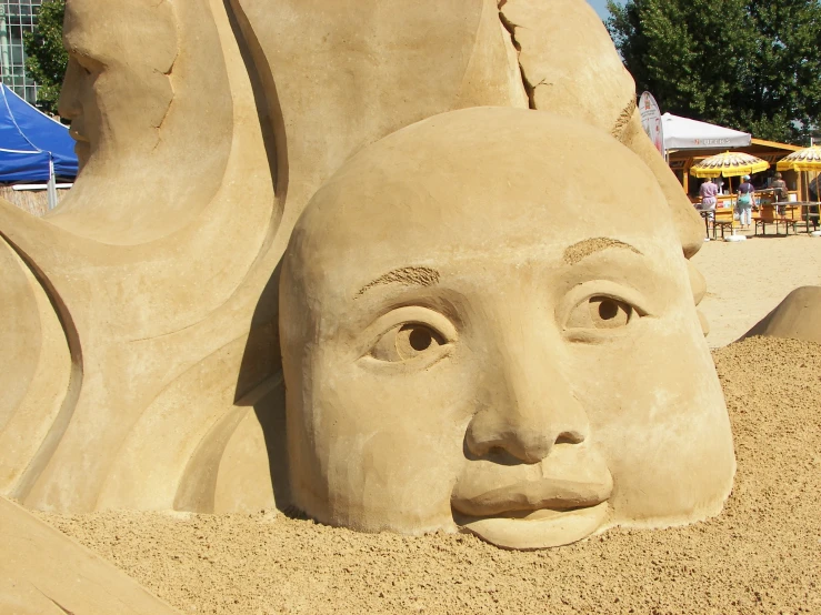 a sculpture of a woman's face and head on a sandy beach