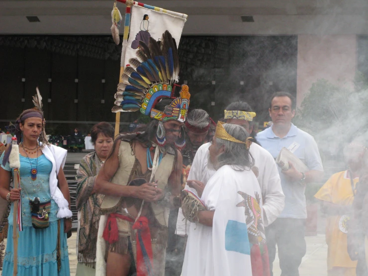 people in native dress are standing and some smoke is rolling