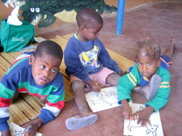 three children sitting on the ground doing crafts