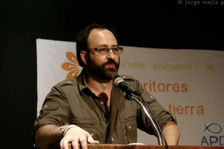 man with glasses at podium making speech in large room