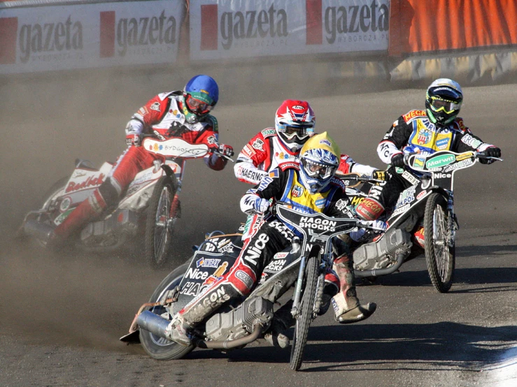 three motorcycle racers kicking up dust and going for a position