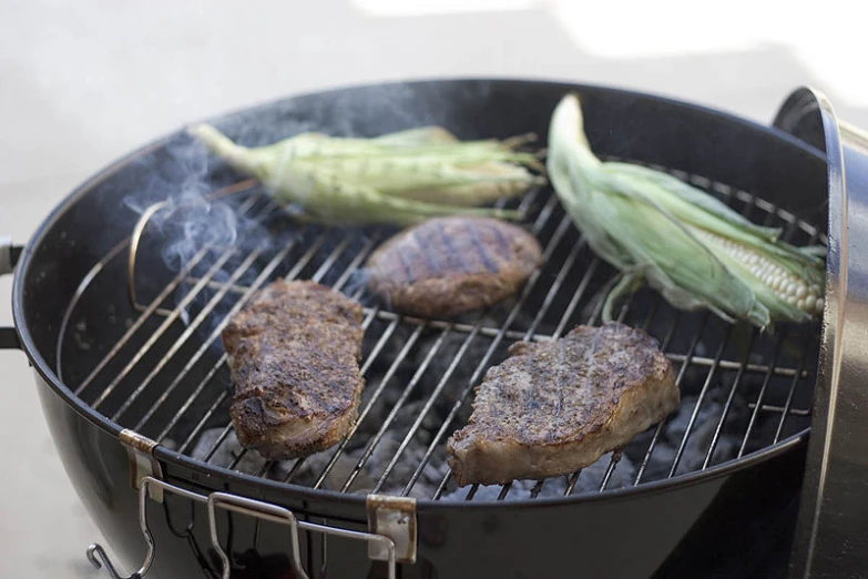 steak and corn on the grill being cooked on a grill