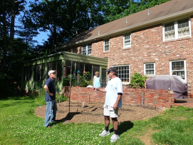 two men talking in front of a brick house