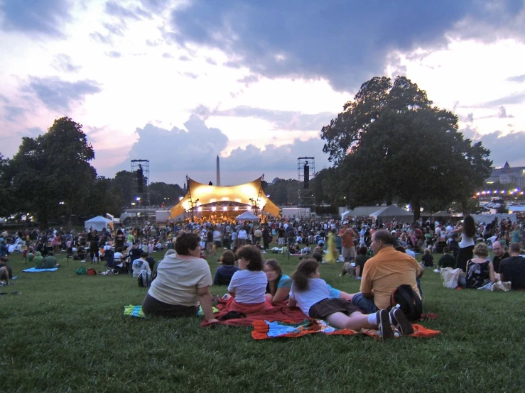 a crowd of people sitting in the grass outside