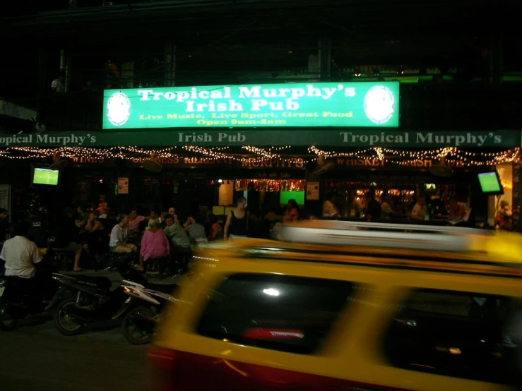 a yellow taxi parked in front of a pub with people eating