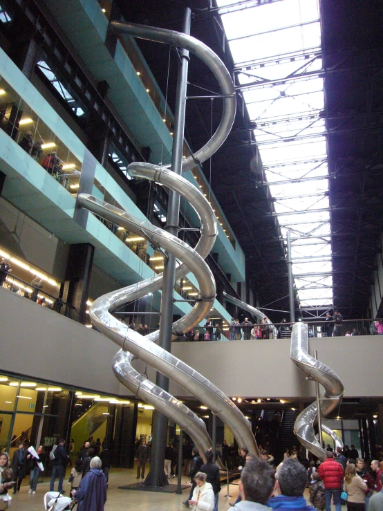 a spiral staircase is in an atrium with lots of people standing around it