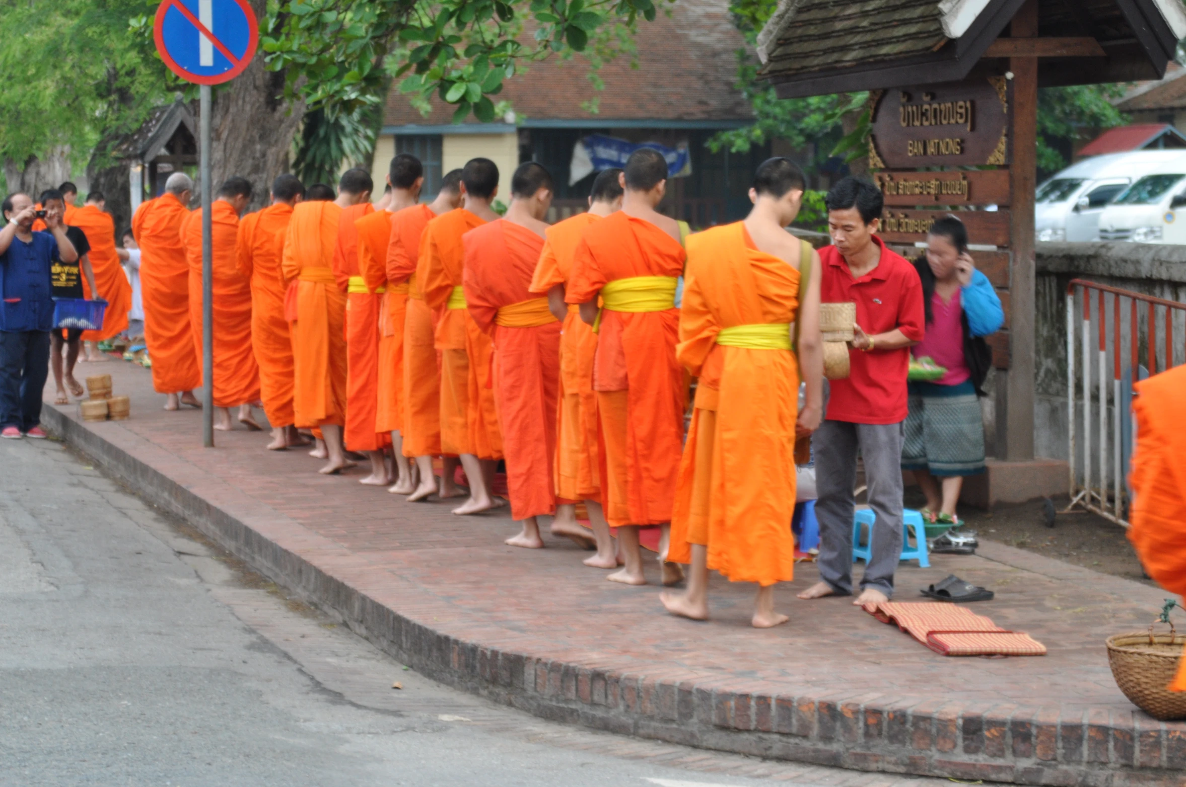 a row of monks in orange robes stand along a street