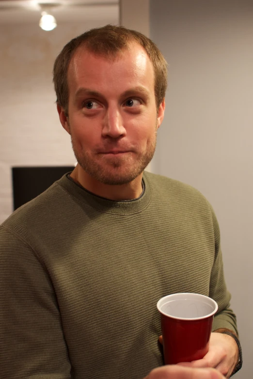 a man holding a cup standing next to a kitchen