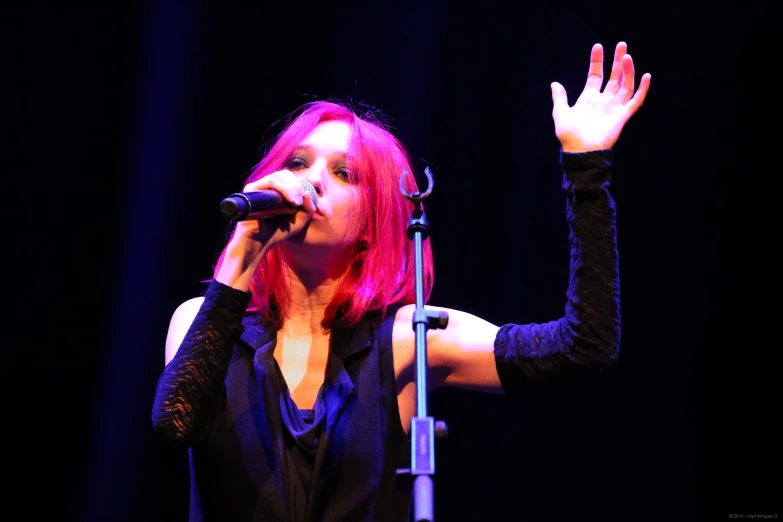 a woman with bright pink hair sings into a microphone