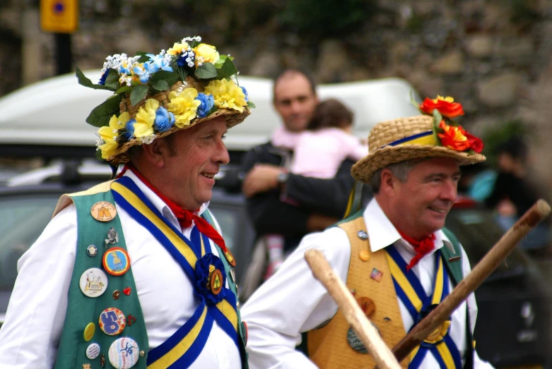 two men with colorful hats are holding sticks