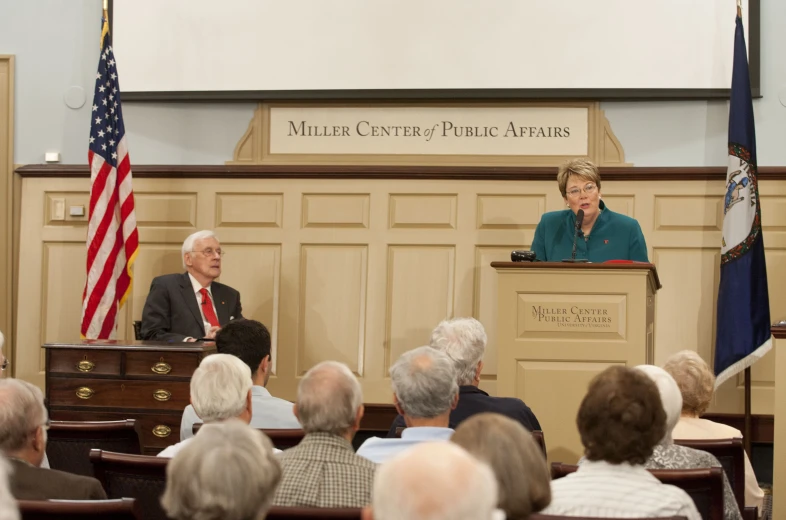 a woman standing at the front of a room talking to a crowd