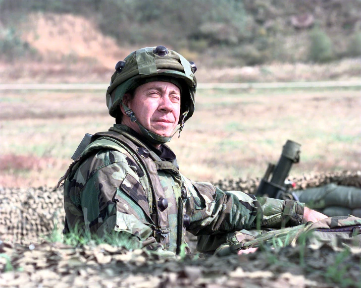 man in camouflage with rifle crouching down in the desert