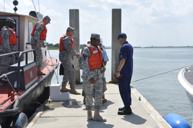 people in camouflage uniforms standing on a dock next to a boat