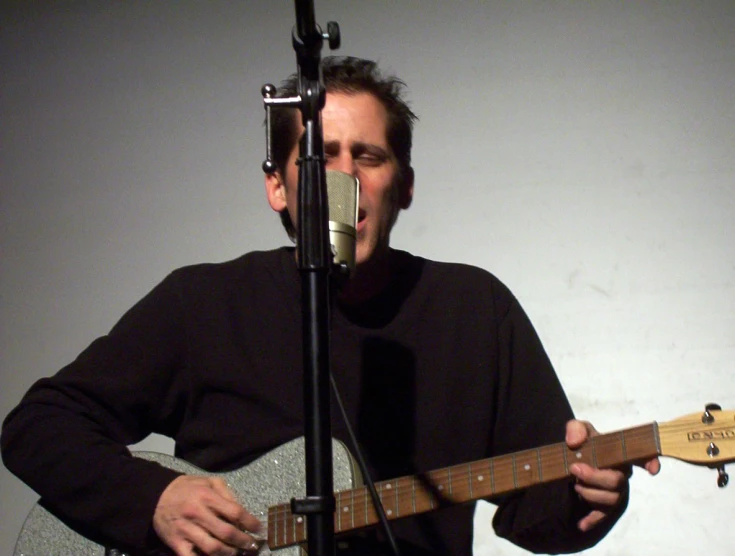 man singing into a microphone while playing the guitar