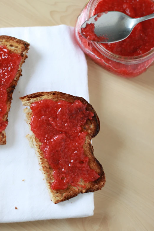 strawberry jam on a piece of bread next to a jar of fruit