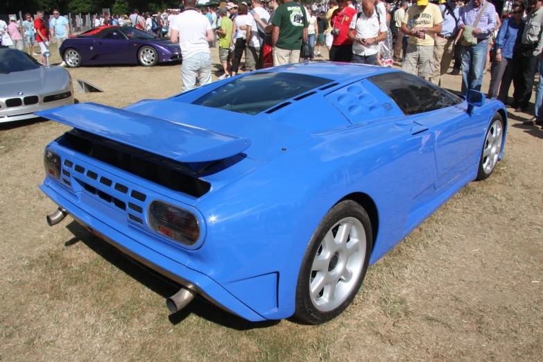 a very blue, modern, supercar sits in the middle of a gathering