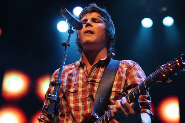 a male in a brown and white shirt is playing guitar