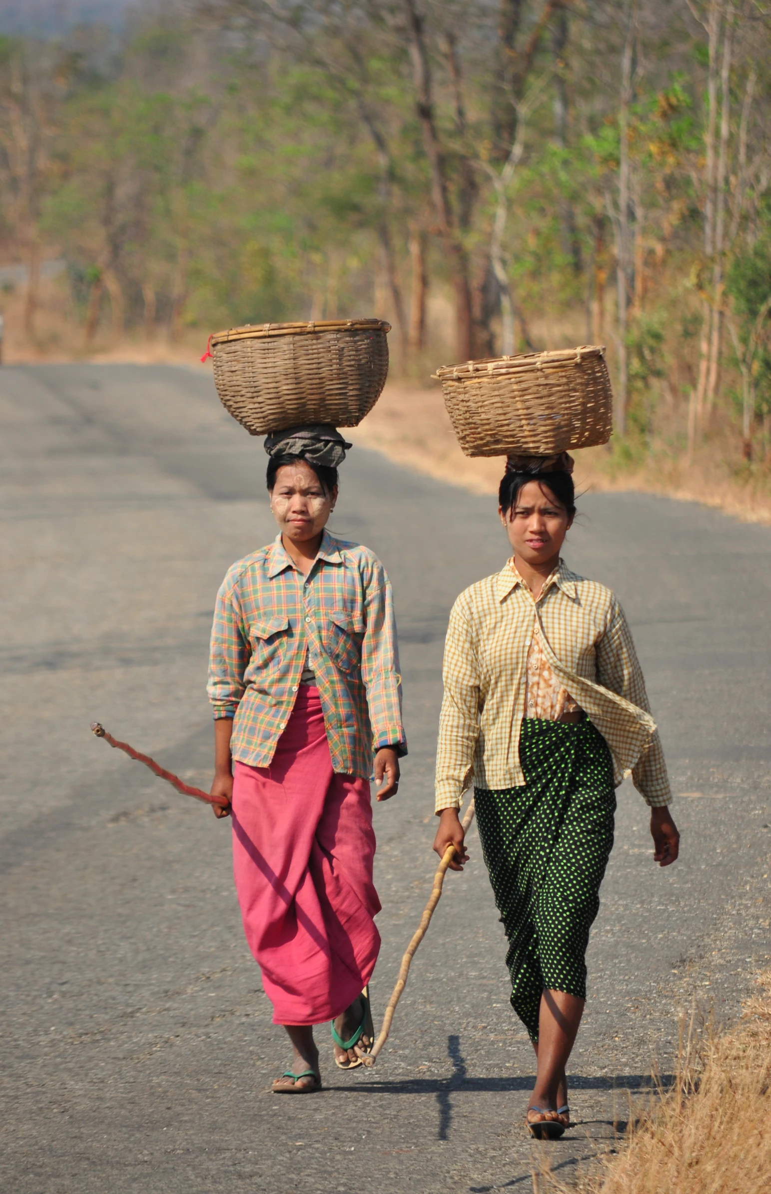 two woman are carrying baskets on their heads and walking