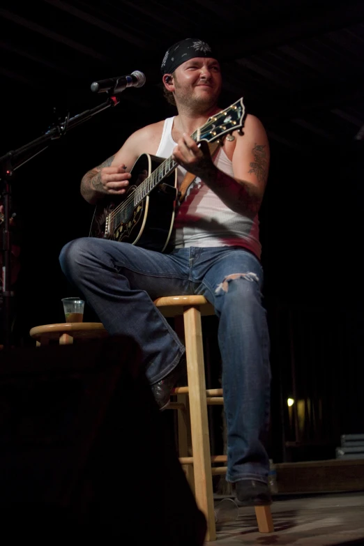 a man sitting on top of a wooden stool with a guitar